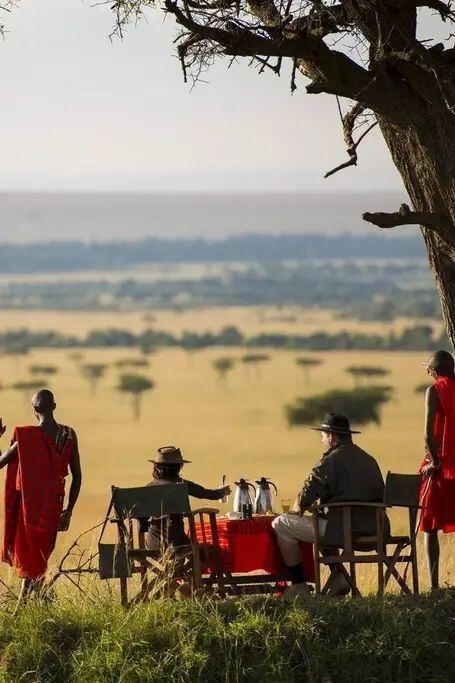 Guests and Maasai hosts at a bush breakfast set beneath a tree overlooking the plains